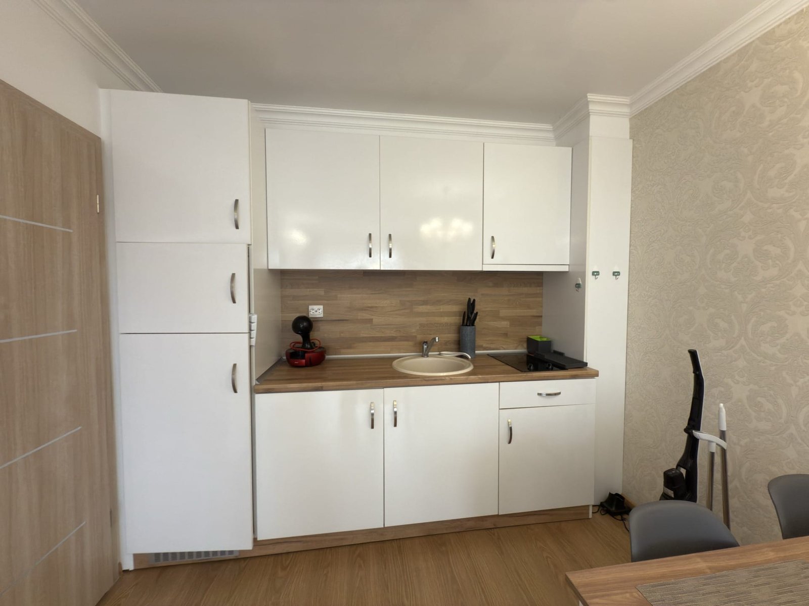 Современная кухня с белыми шкафчиками, деревянной столешницей, раковиной и кухонной техникой в апартаменте.