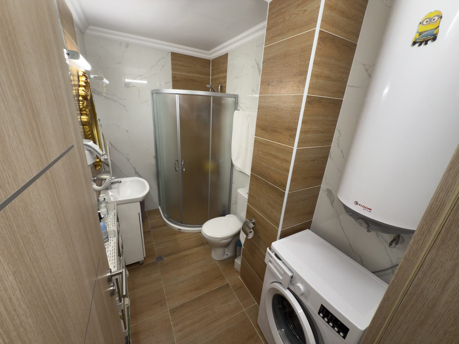 Современная ванная комната с душевой кабиной, стиральной машиной и умывальником, выполненная в нейтральных тонах.