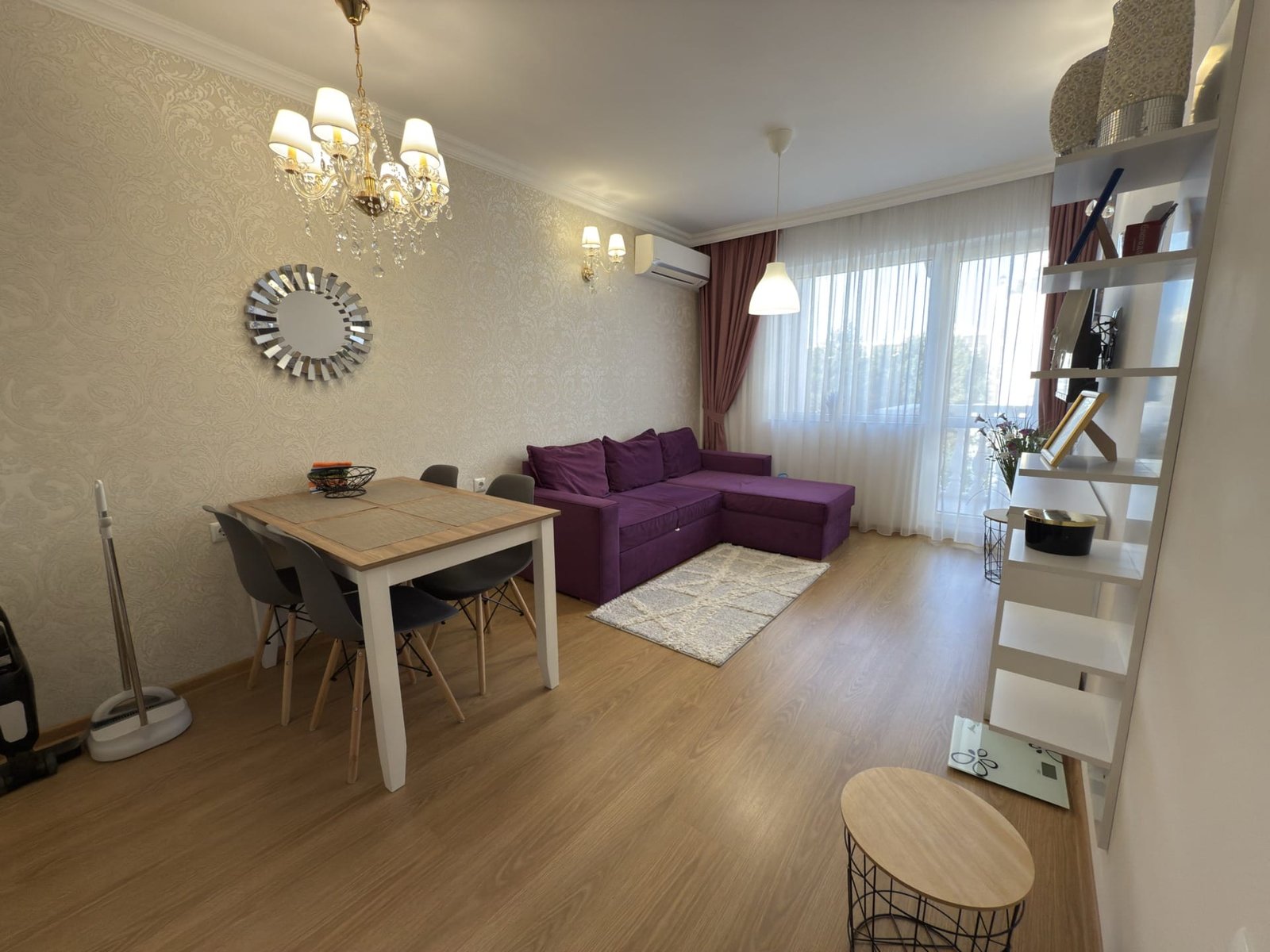 Современный интерьер трехкомнатного апартамента: стильная гостиная с фиолетовым диваном, обеденным столом и ярким освещением.