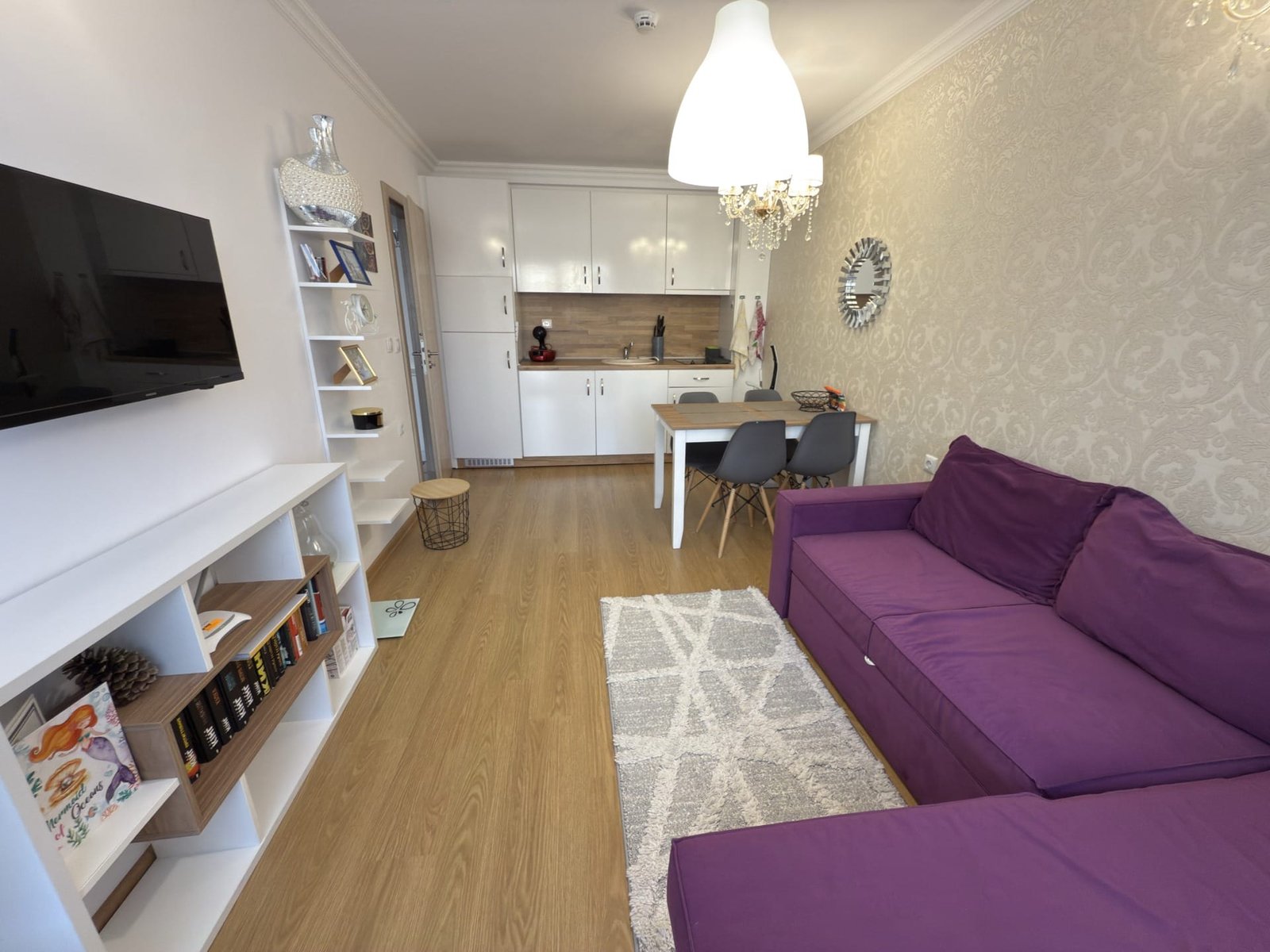 Современный трехкомнатный апартамент с фиолетовым диваном, обеденной зоной и светлым интерьером. Уютная атмосфера и стильный декор.