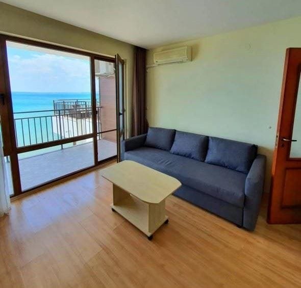 Современный интерьер трехкомнатного апартамента с диваном и столом, выходящим на балкон с видом на море.