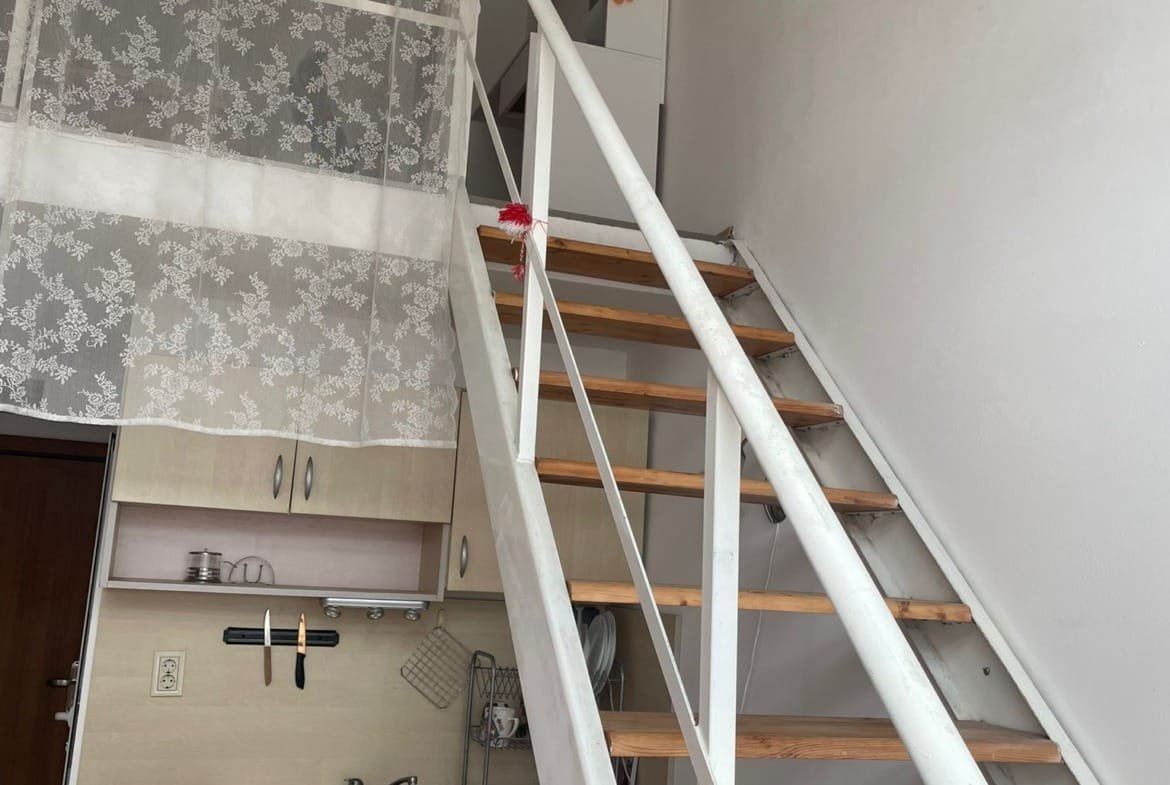 Современная квартира с лестницей, кухней и стиральной машиной, оформленная в светлых тонах и с текстильными элементами.