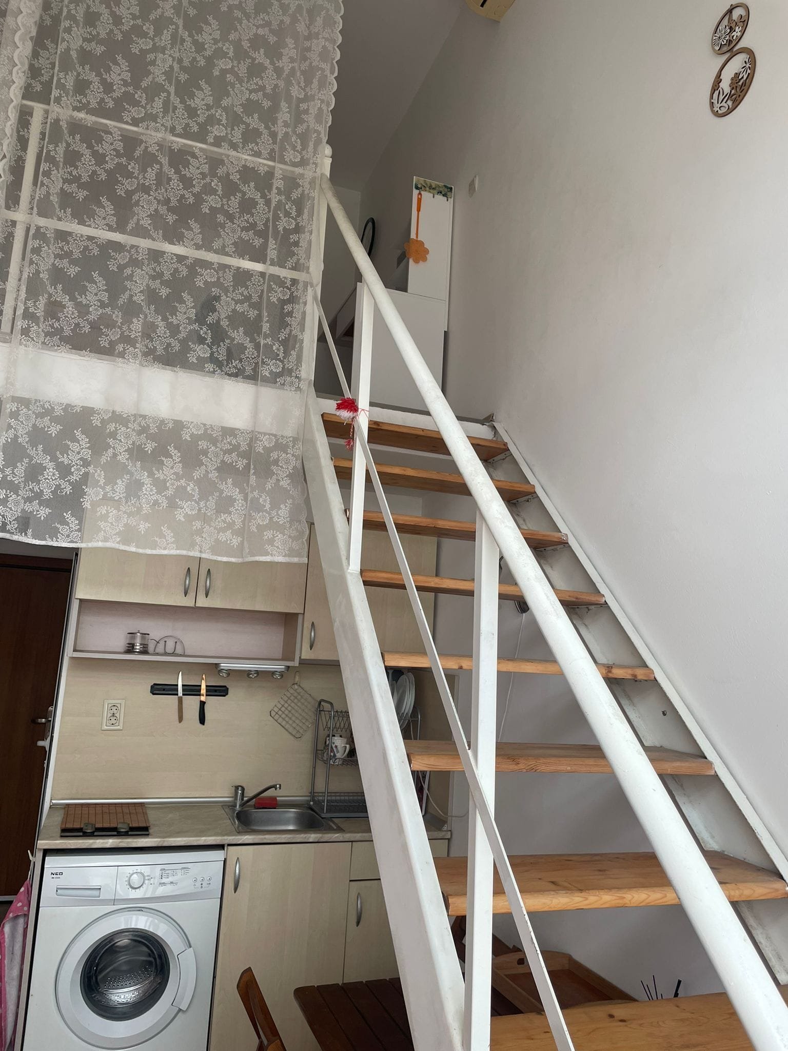 Современная квартира с лестницей, кухней и стиральной машиной, оформленная в светлых тонах и с текстильными элементами.