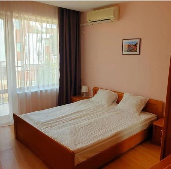 Двуспальная кровать с белым постельным бельем в светлой комнате с балконом, мягкими шторами и вентилятором.