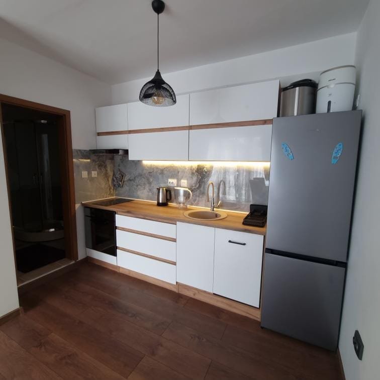 Современная кухня в студии с мебелью белого цвета, серой столешницей, встроенной техникой и светлой отделкой стен.