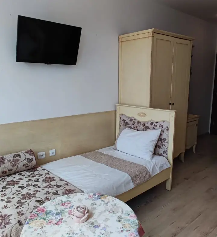 Комната с одной кроватью и двумя местами для сидения, светлые тона, уютная обстановка, телевизор на стене.