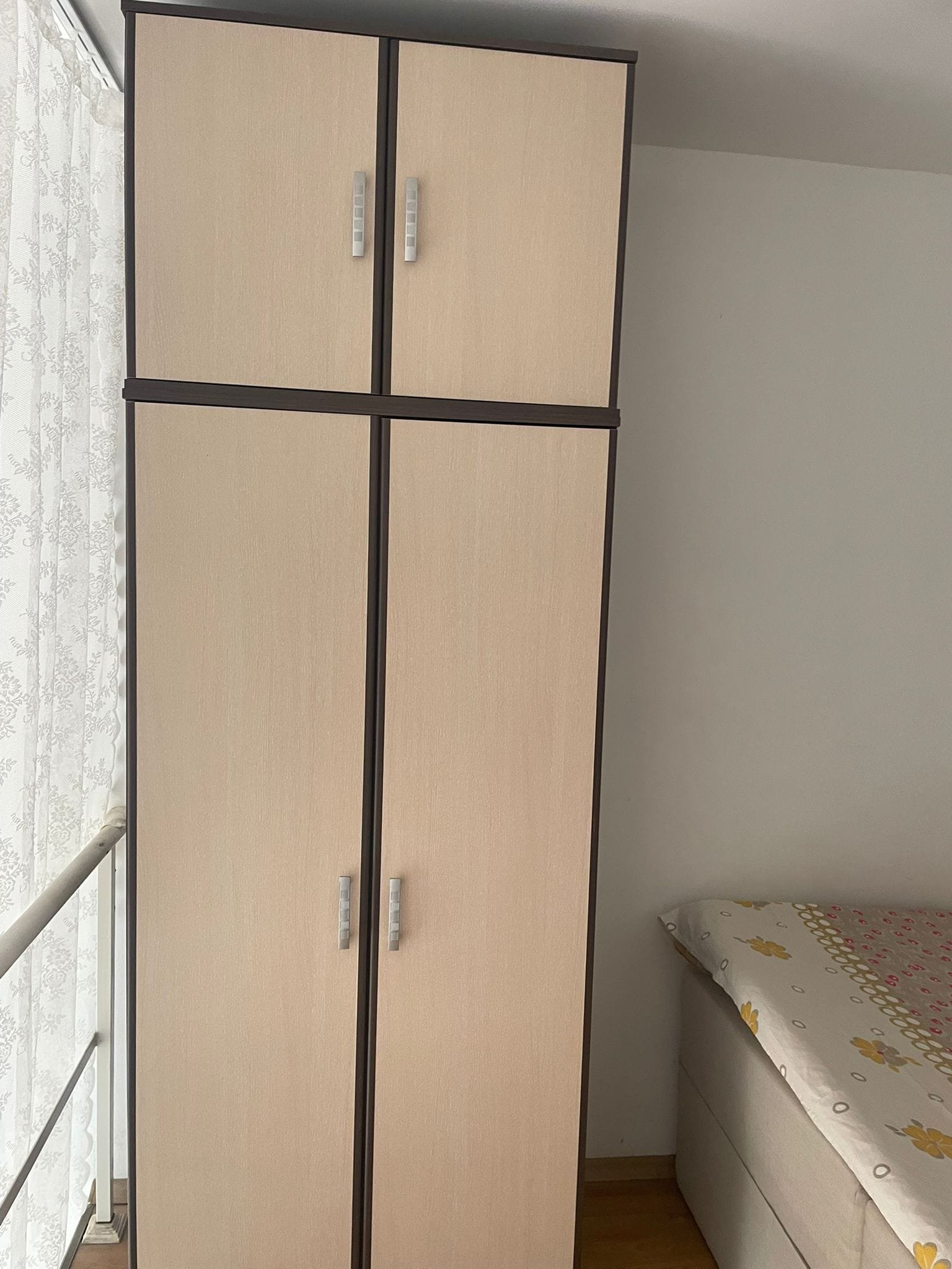 Деревянный шкаф светлого цвета с четырьмя дверцами рядом с кроватью и окнами с занавесками.