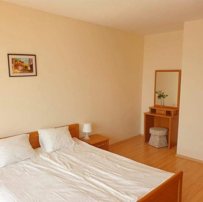 Современная спальня с двуспальной кроватью, светлыми стенами, тумбочкой и столиком с зеркалом. Спокойная атмосфера.