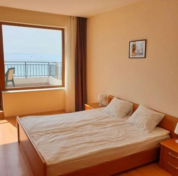 Светлая спальня с двуспальной кроватью, выходом на балкон и видом на море. Стены светлые, деревянный пол.