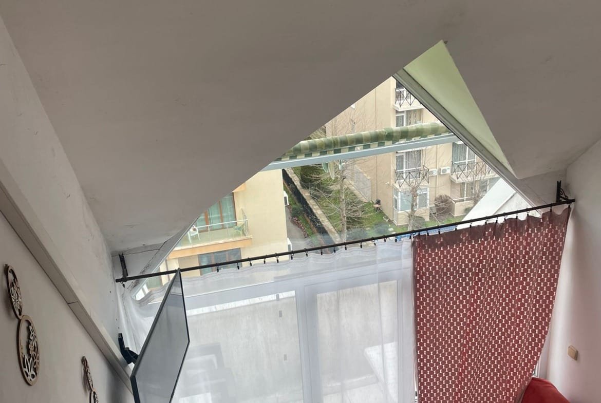 Современная студия с угловым окном, яркими шторами и красным диваном, создающая уютную атмосферу.