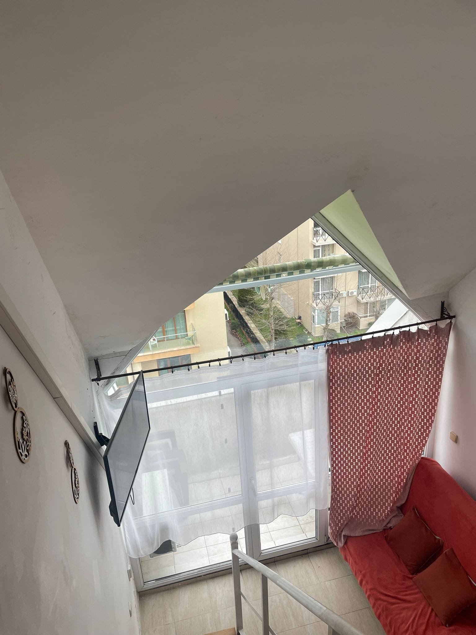 Современная студия с угловым окном, яркими шторами и красным диваном, создающая уютную атмосферу.