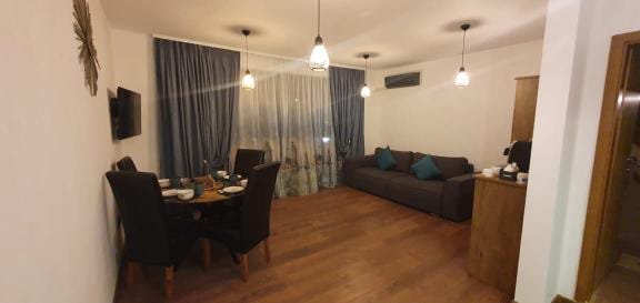 Современная студия с уютной мебелью, столом и стульями, мягким диваном и большими окнами, оформленная в спокойных тонах.