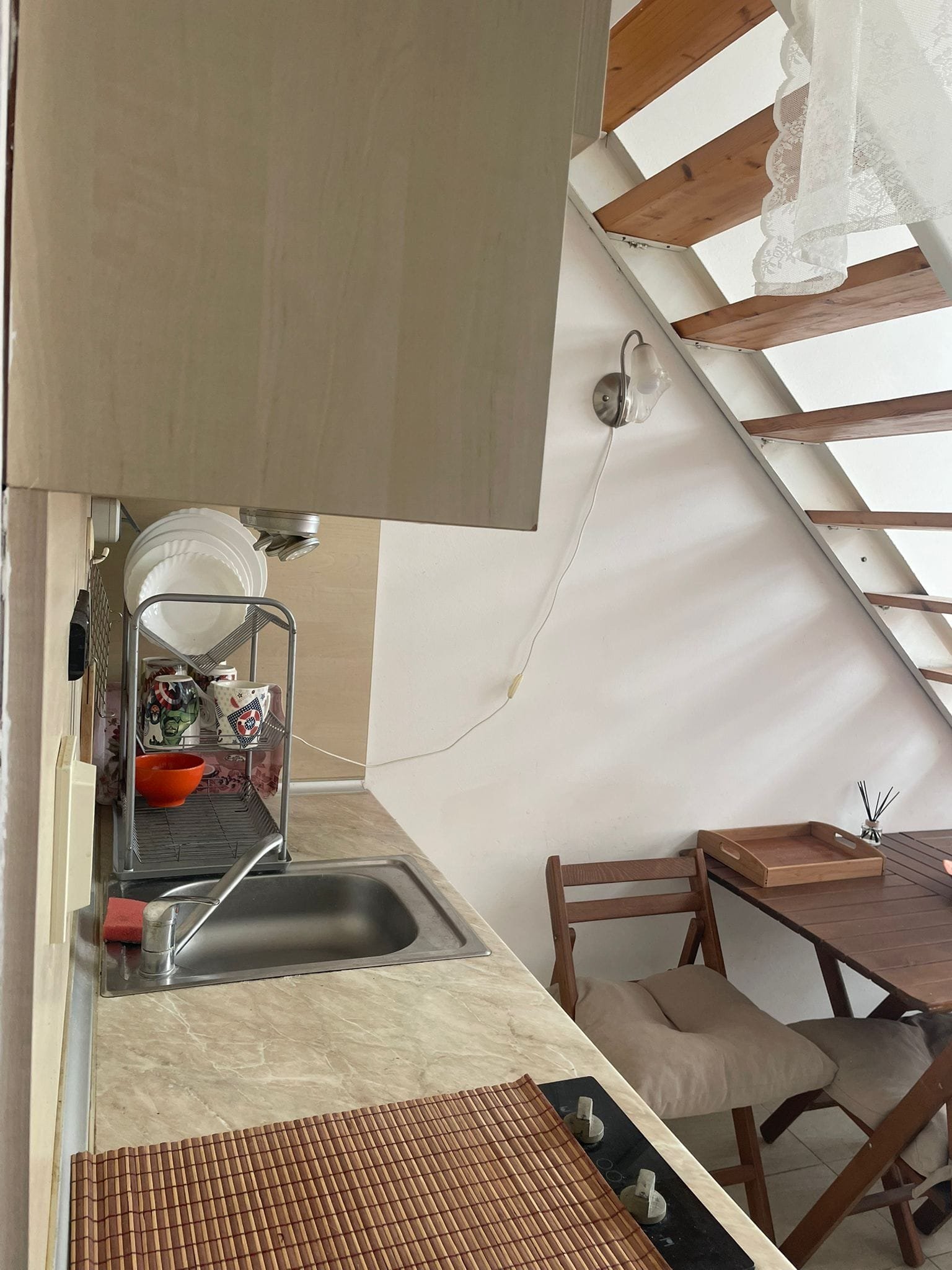 Кухонный уголок в студии с мойкой, деревянной лестницей и столом с предметами быта. Классический дизайн, уютная атмосфера.