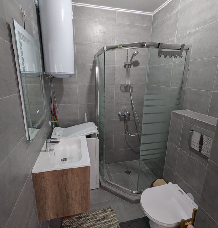 Современная ванная комната с душевой кабиной, туалетом, раковиной и стильной отделкой в нейтральных тонах.