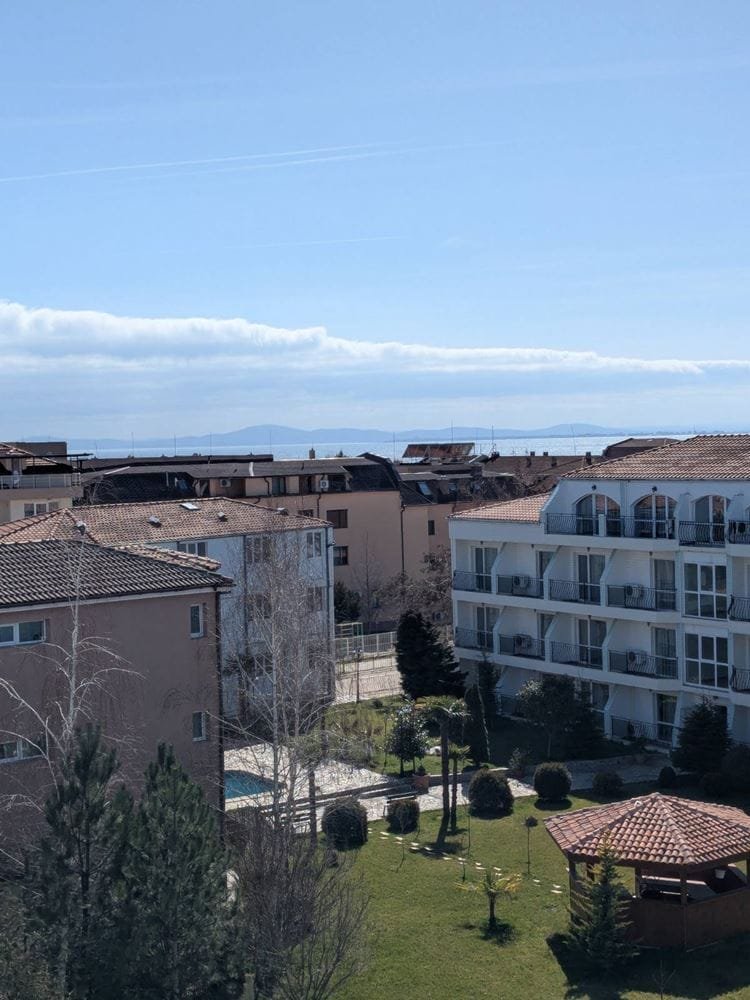 Двухкомнатный апартамент с видом на море и крыши зданий, зеленый двор с растениями и прогулочными дорожками.