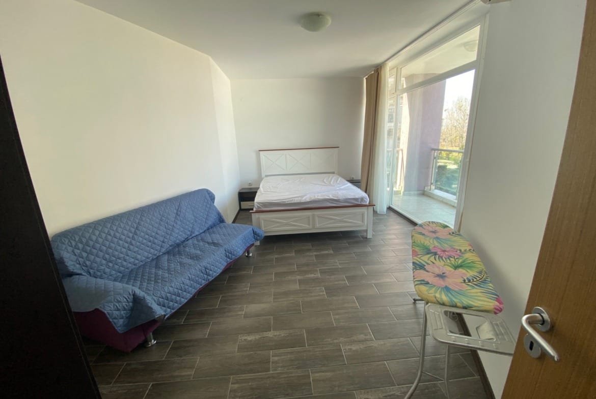 Современная комната с односпальной кроватью, диваном и гладильной доской, выход на балкон с видом на окружающую природу.