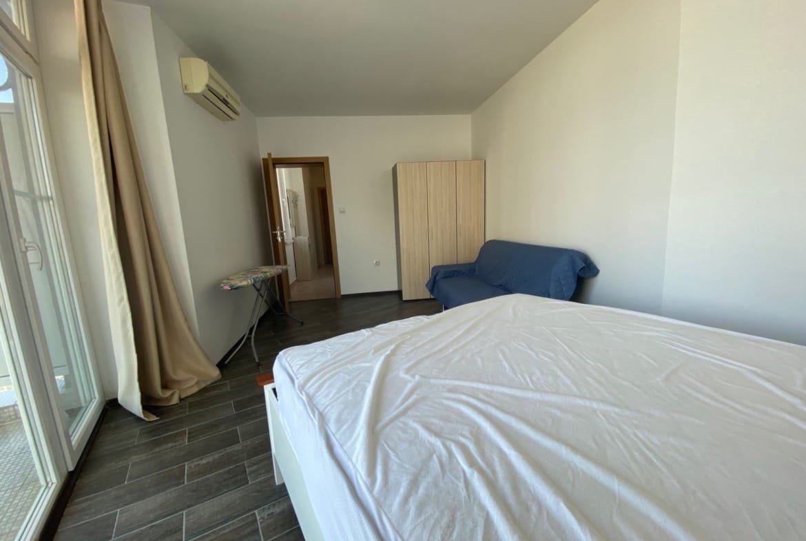 Современный светлый интерьер трехкомнатного апартамента, с кроватью, диваном и большой застекленной дверью.