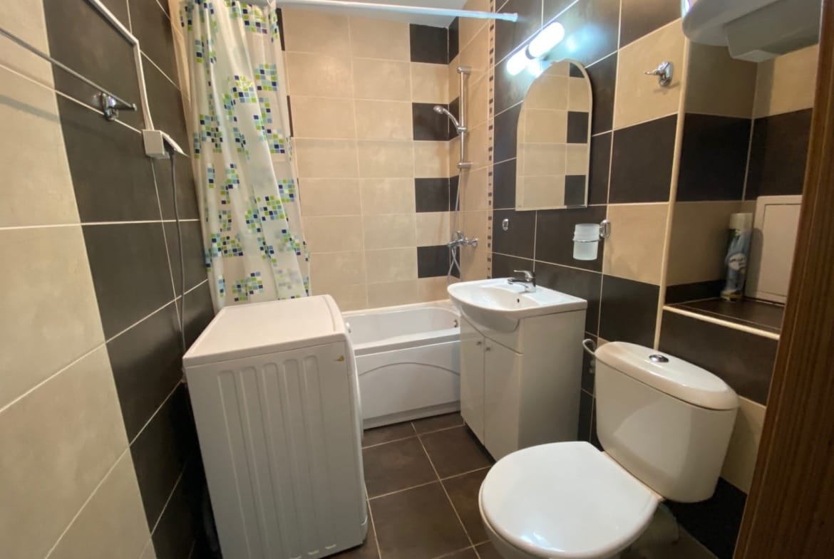 Современная ванная комната с ванной, стиральной машиной и умывальником, оформленная в светло-темных тонах.