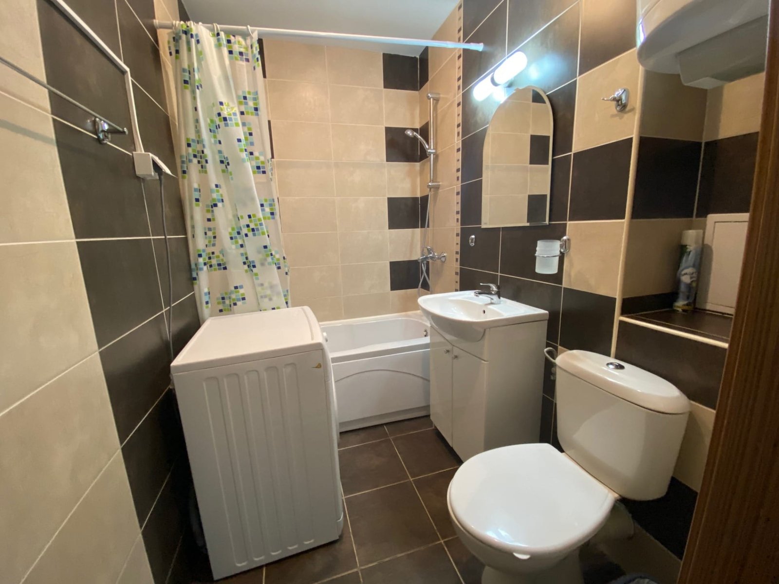 Современная ванная комната с ванной, стиральной машиной и умывальником, оформленная в светло-темных тонах.