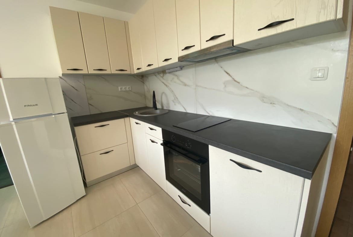 Современная кухня в трёхкомнатном апартаменте с белыми и серыми шкафами, чёрной столешницей и бытовой техникой.