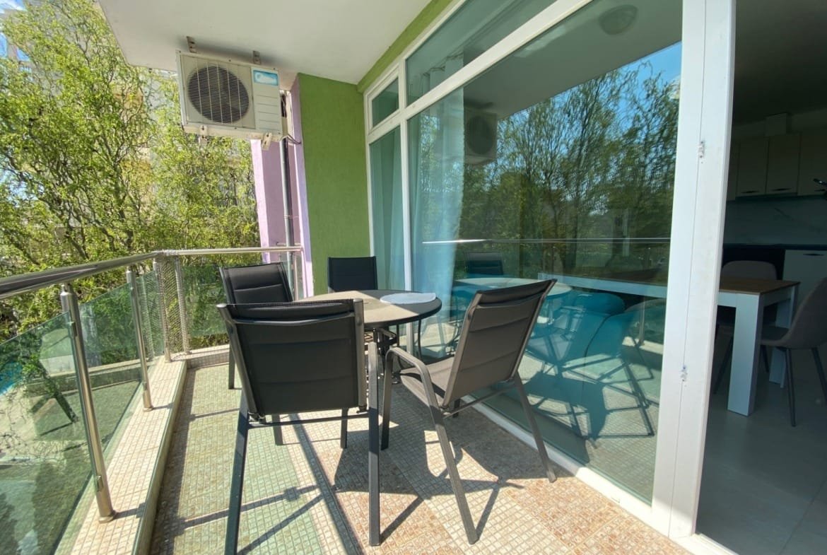 Балкон с обеденным столом и стульями, зелеными стенами и большими окнами, предлагающий вид на окружающую растительность.