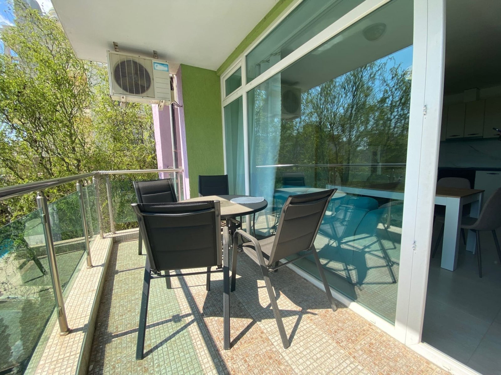 Балкон с обеденным столом и стульями, зелеными стенами и большими окнами, предлагающий вид на окружающую растительность.