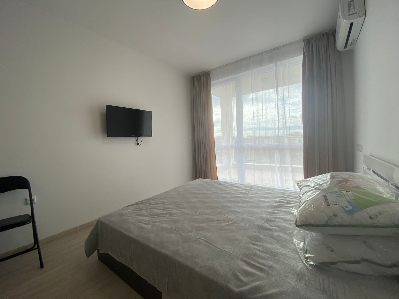 Современная студия в комплексе с кроватью, телевизором и панорамными окнами, оформленная в светлых тонах.