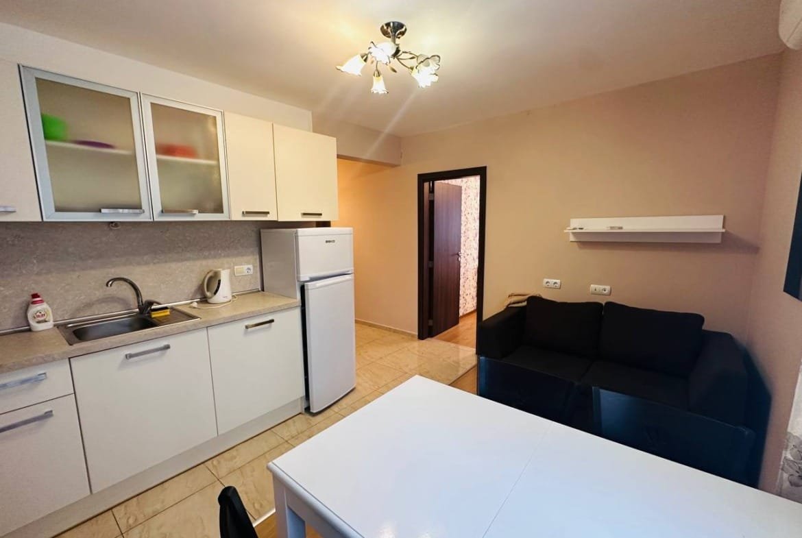 Современная кухня в трехкомнатном апартаменте с обеденным столом, холодильником и диваном, светлые тона интерьера.