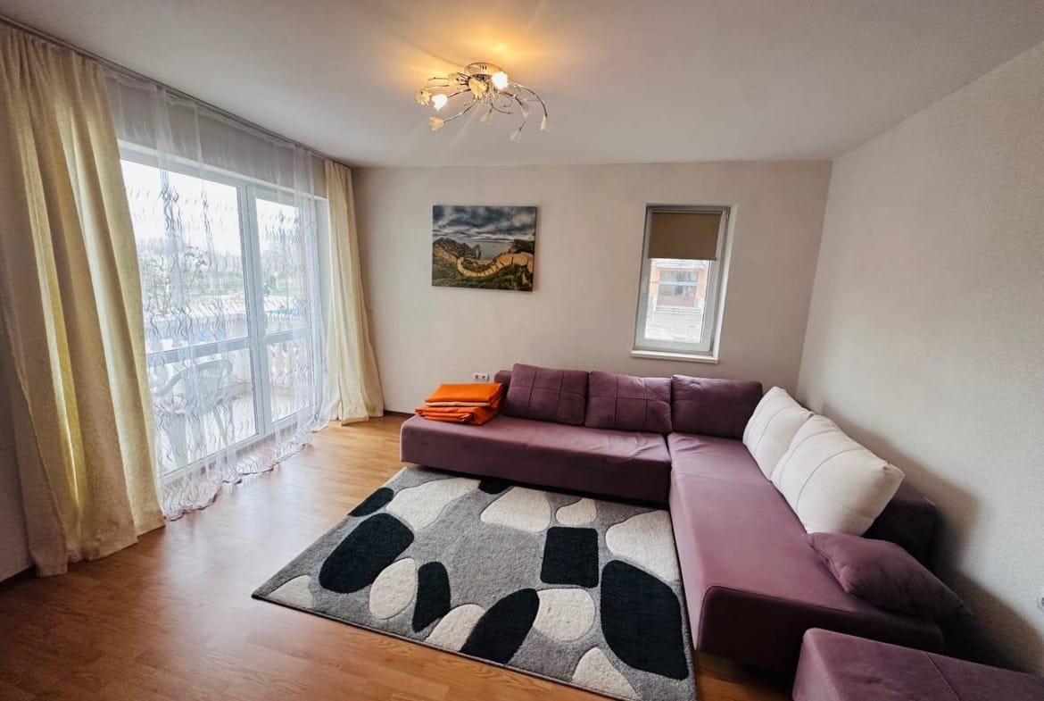 Современный светлый интерьер трехкомнатного апартамента с уютным фиолетовым диваном и большим окном.