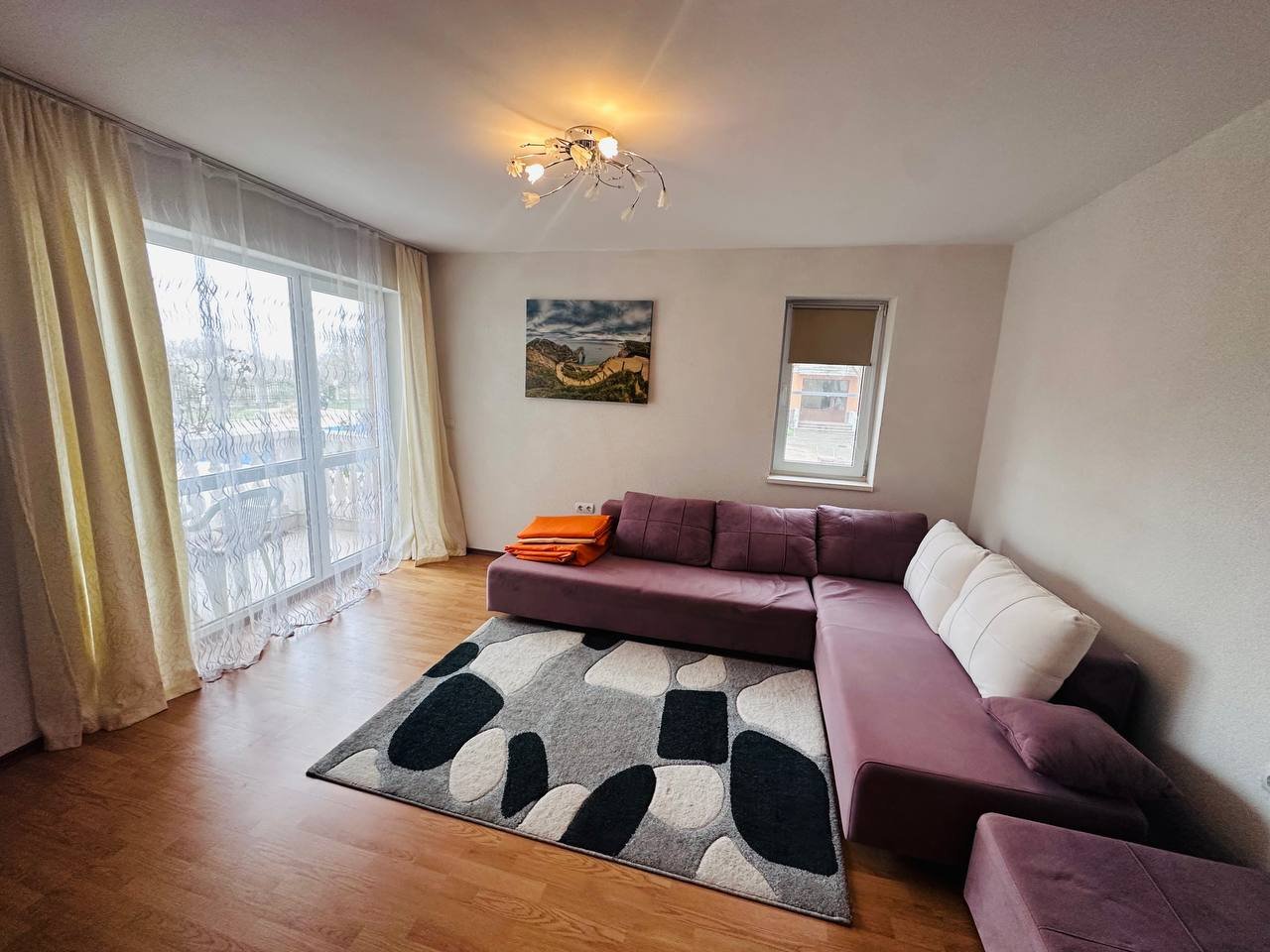 Современный светлый интерьер трехкомнатного апартамента с уютным фиолетовым диваном и большим окном.