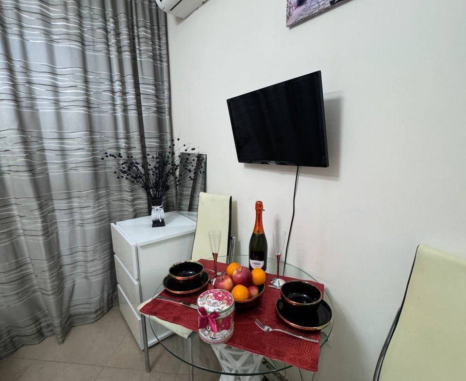 Студия с угловым обеденным столом, столовыми приборами и бокалом шампанского, оформленная в светлых тонах.