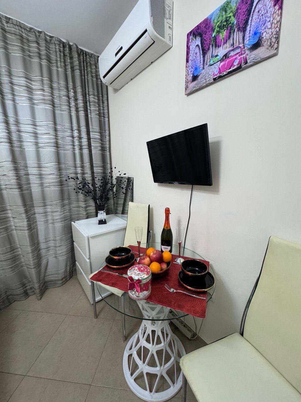 Студия с угловым обеденным столом, столовыми приборами и бокалом шампанского, оформленная в светлых тонах.