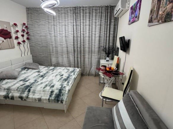 Современная студия с двуспальной кроватью, диваном, столиком и декоративными элементами на стенах.