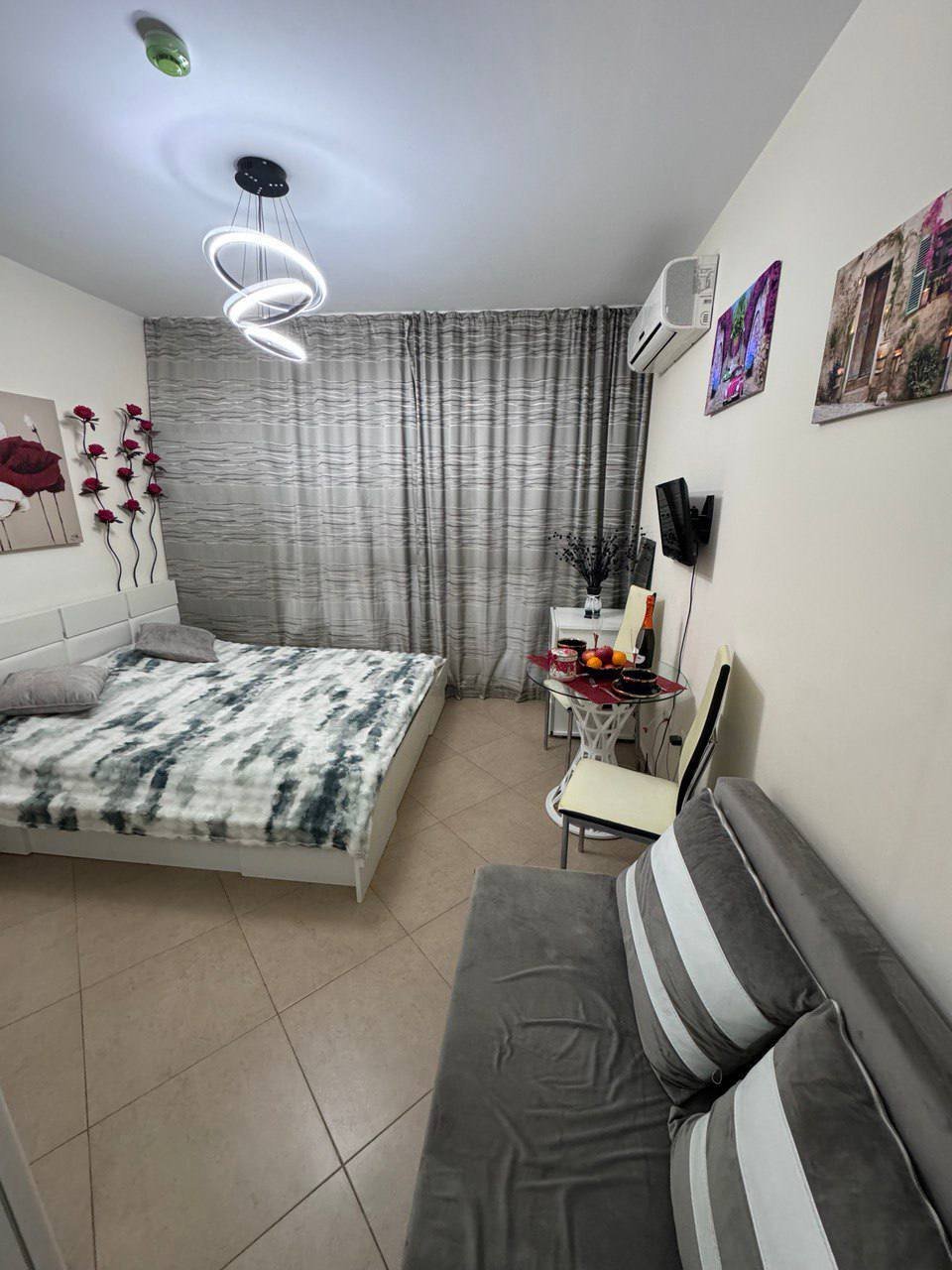 Современная студия с двуспальной кроватью, диваном, столиком и декоративными элементами на стенах.