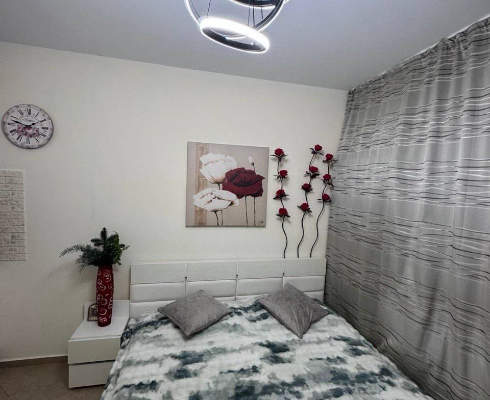 Современная спальня с белой кроватью, стильным освещением и декоративными цветами на стенах, оформленная в нежных тонах.