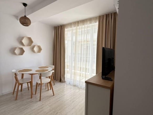 Современная студия с обеденной зоной, светлыми тонами и большими окнами, создающими уютную атмосферу.