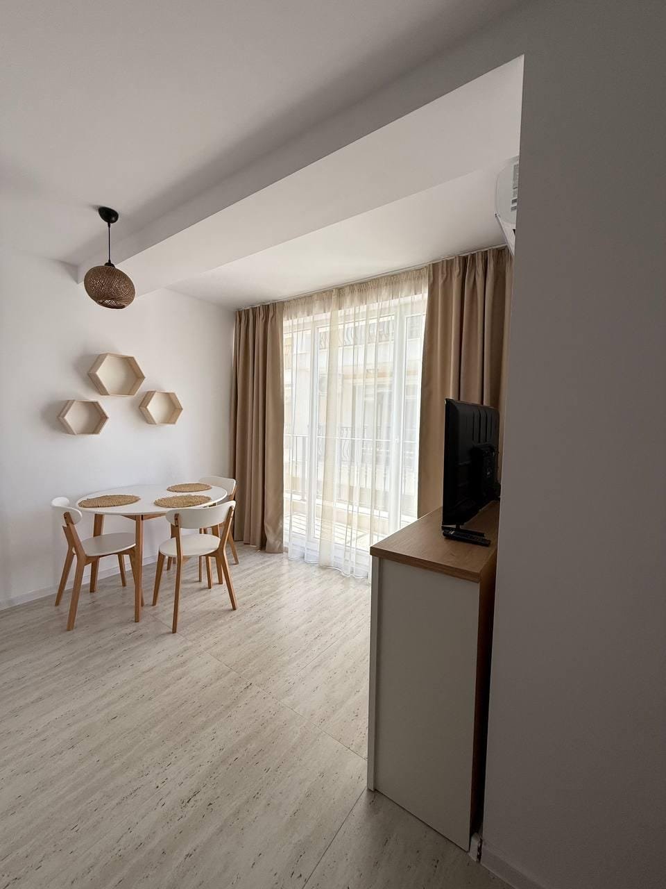 Современная студия с обеденной зоной, светлыми тонами и большими окнами, создающими уютную атмосферу.