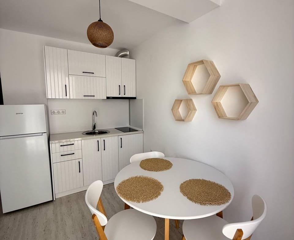 Современная кухня с обеденным столом и четырьмя стульями, белые стены, светлые деревянные детали, элементы декора.