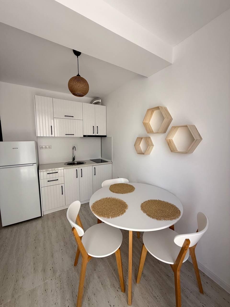 Современная кухня с обеденным столом и четырьмя стульями, белые стены, светлые деревянные детали, элементы декора.