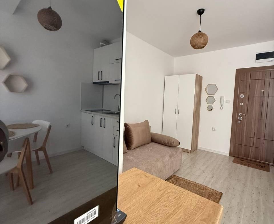 Интерьер студии с телевизором, кухонной зоной и мягким диваном, светлые тона и уютная обстановка.