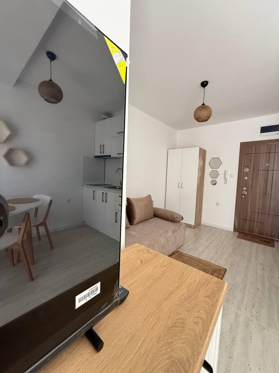 Интерьер студии с телевизором, кухонной зоной и мягким диваном, светлые тона и уютная обстановка.