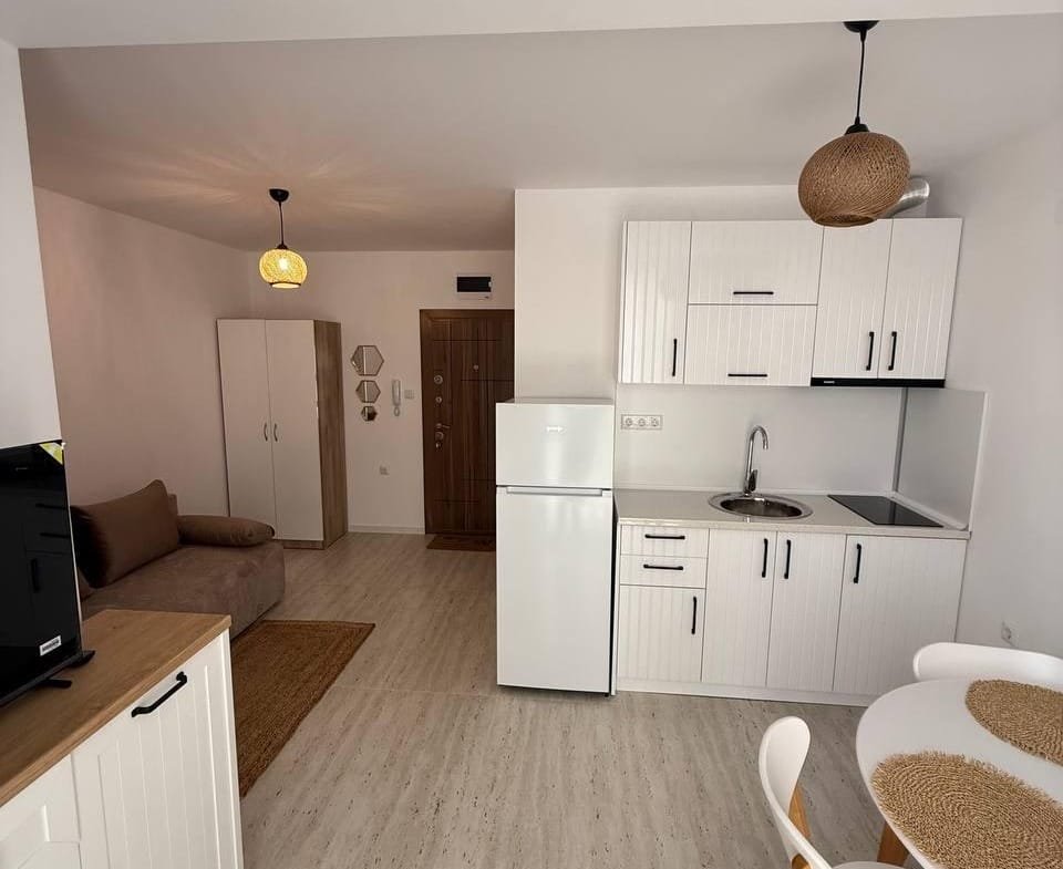 Современная студия с кухней, обеденным столом и диваном, оформленная в светлых тонах, в комплексе Villa Grand.