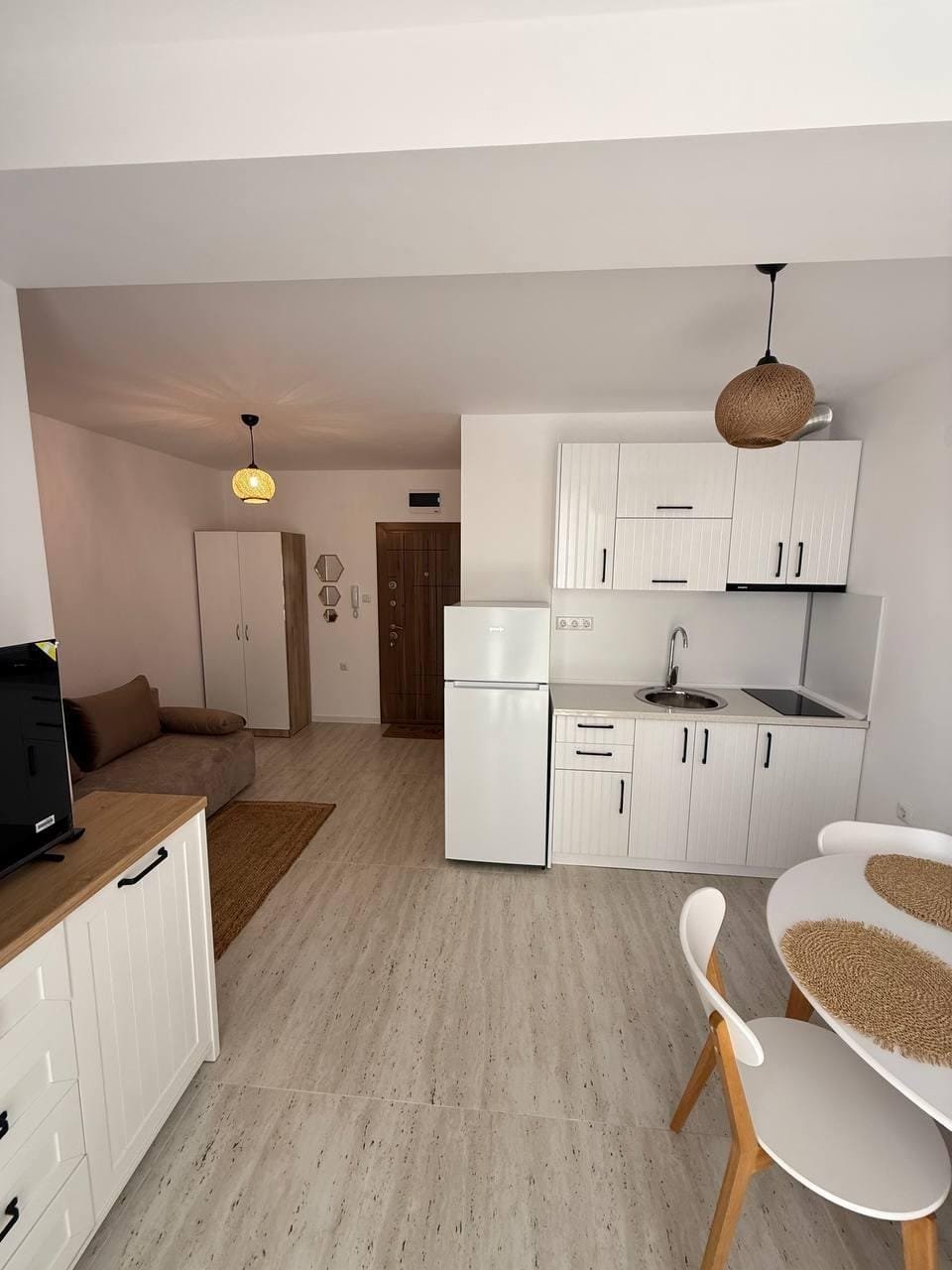 Современная студия с кухней, обеденным столом и диваном, оформленная в светлых тонах, в комплексе Villa Grand.