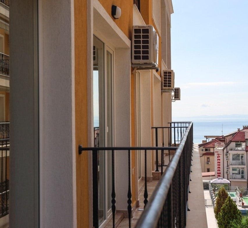 Балкон с перилами, выходящий на море, с квартирой в жилом комплексе, оформленной в светлых тонах.