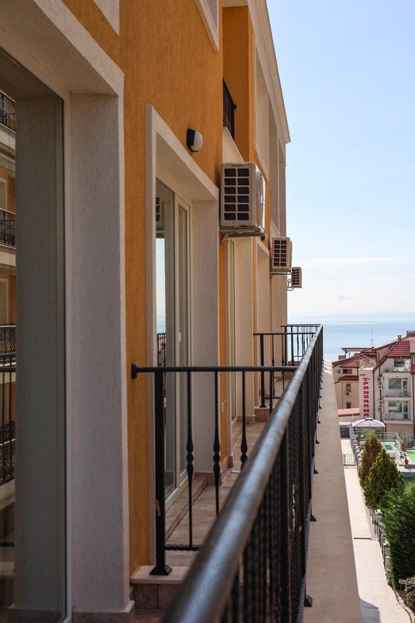 Балкон с перилами, выходящий на море, с квартирой в жилом комплексе, оформленной в светлых тонах.