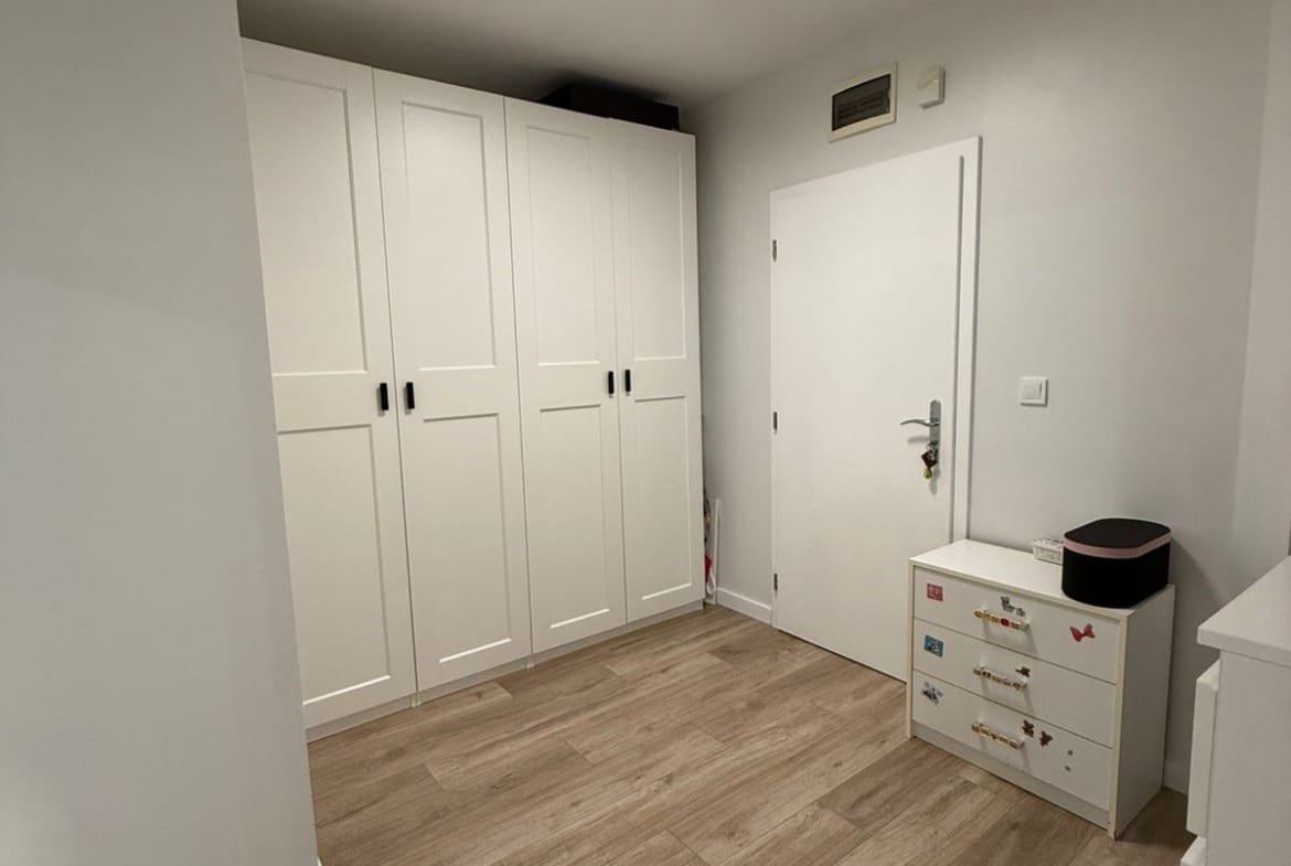 Современный интерьер двухкомнатного апартамента с белыми шкафами и светлым деревянным полом. Просторная и светлая комната.