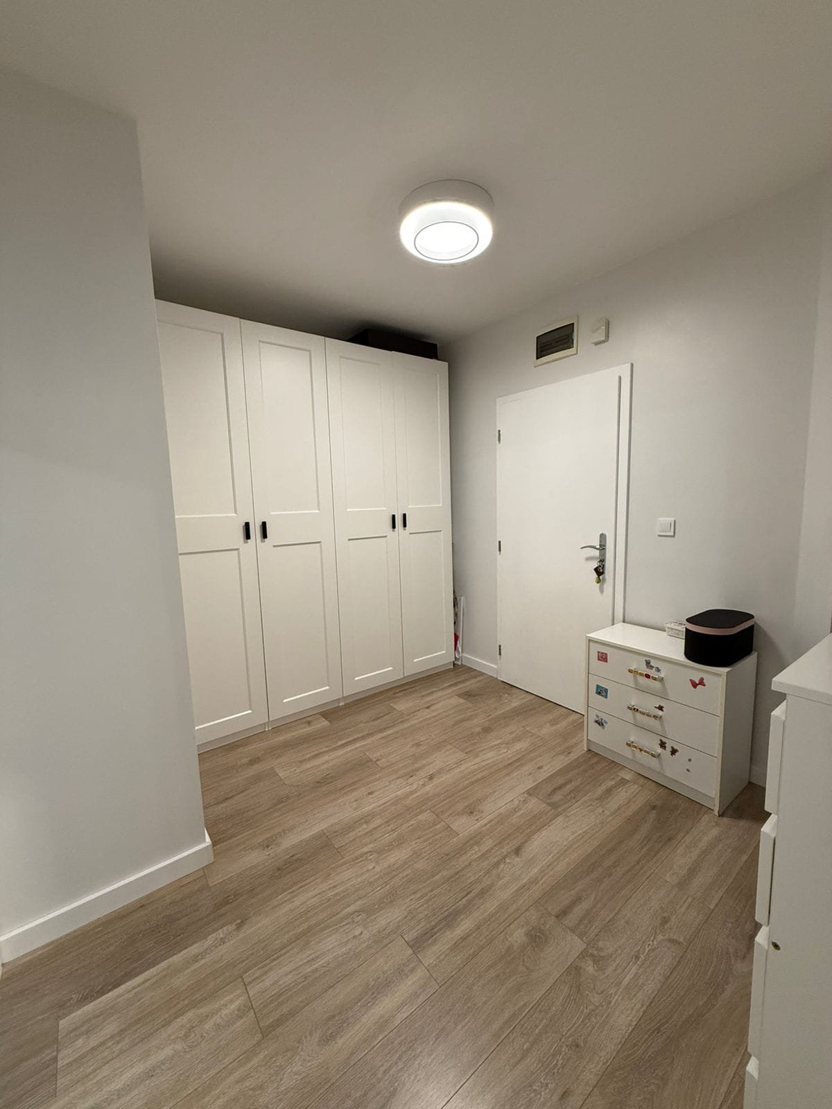 Современный интерьер двухкомнатного апартамента с белыми шкафами и светлым деревянным полом. Просторная и светлая комната.