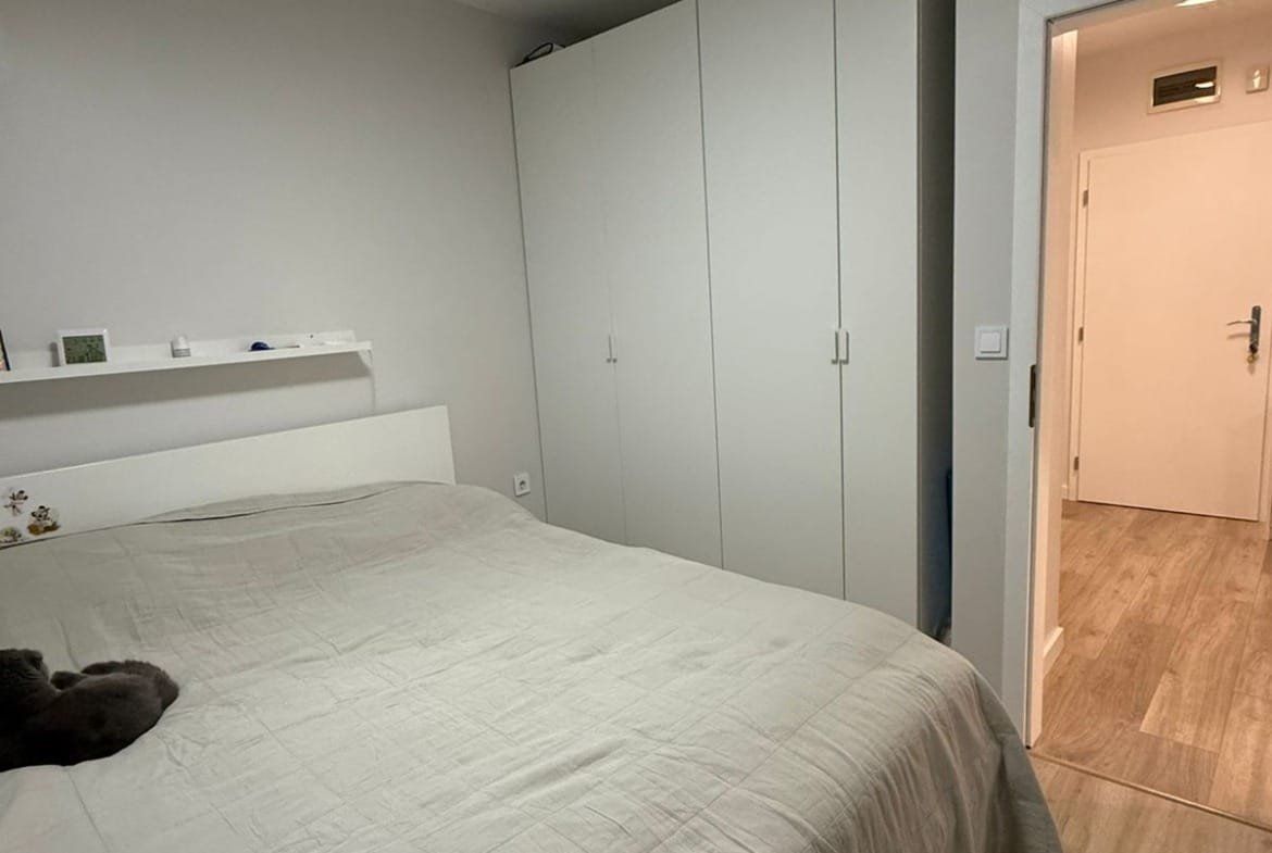 Современная спальня с двуспальной кроватью, белым шкафом и светлым интерьером в апартаменте.