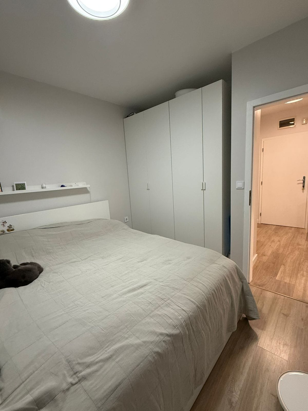 Современная спальня с двуспальной кроватью, белым шкафом и светлым интерьером в апартаменте.