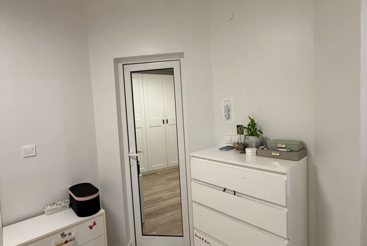 Двухкомнатный апартамент с белыми стенами, светлым полом, зеркалом и комодом, оформленным в современном стиле.